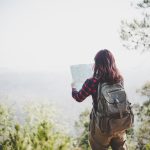 Back side of traveler girl searching right direction on map, while traveling to hiking in the mountain. Travel concept.