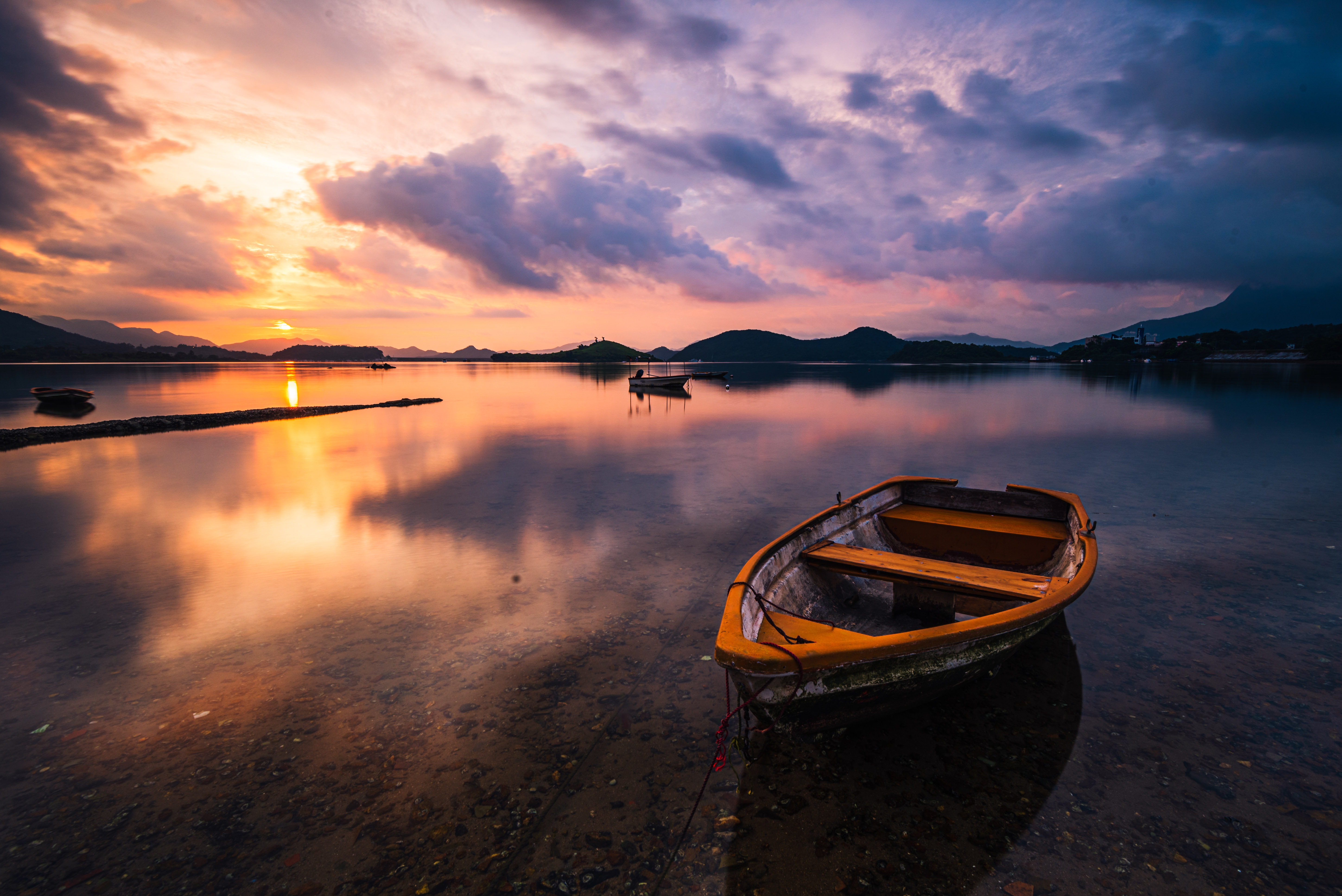 A beautiful shot of a small lake with a wooden rowboat in focus and breathtaking clouds in the sky