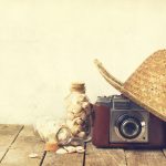Summer or vacation concept. Straw hat with old vintage camera and shells on wooden background.