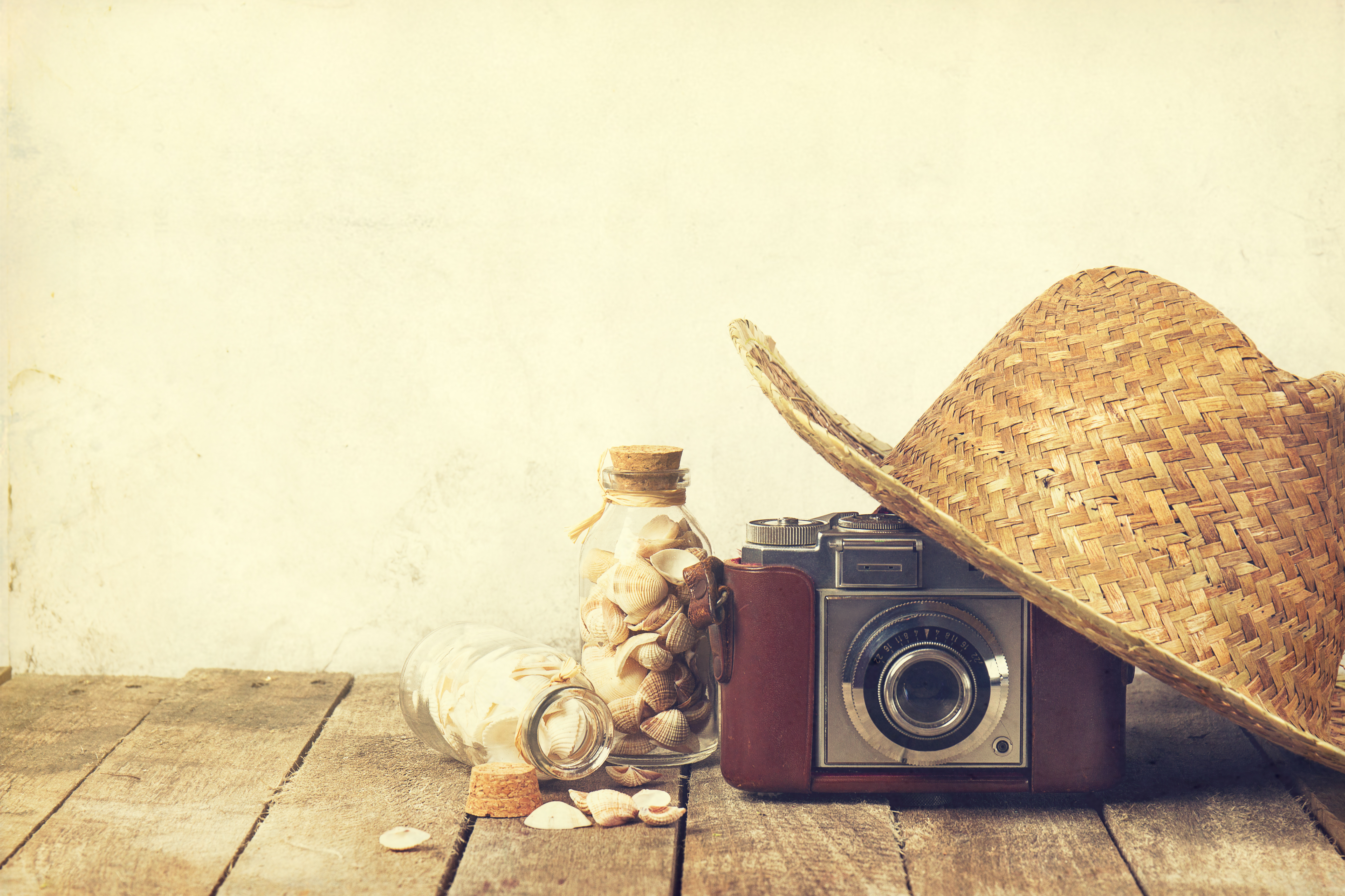 Summer or vacation concept. Straw hat with old vintage camera and shells on wooden background.