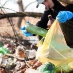 Man in gloves collecting scattered plastic bottles from the ground in the nature