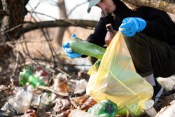Man in gloves collecting scattered plastic bottles from the ground in the nature